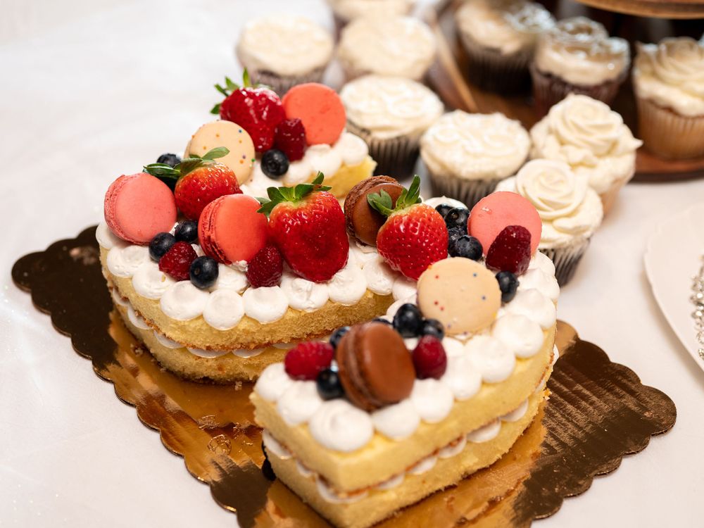 Heart-shaped cream cake decorated with fresh strawberries, macarons, and berries on a golden serving board.