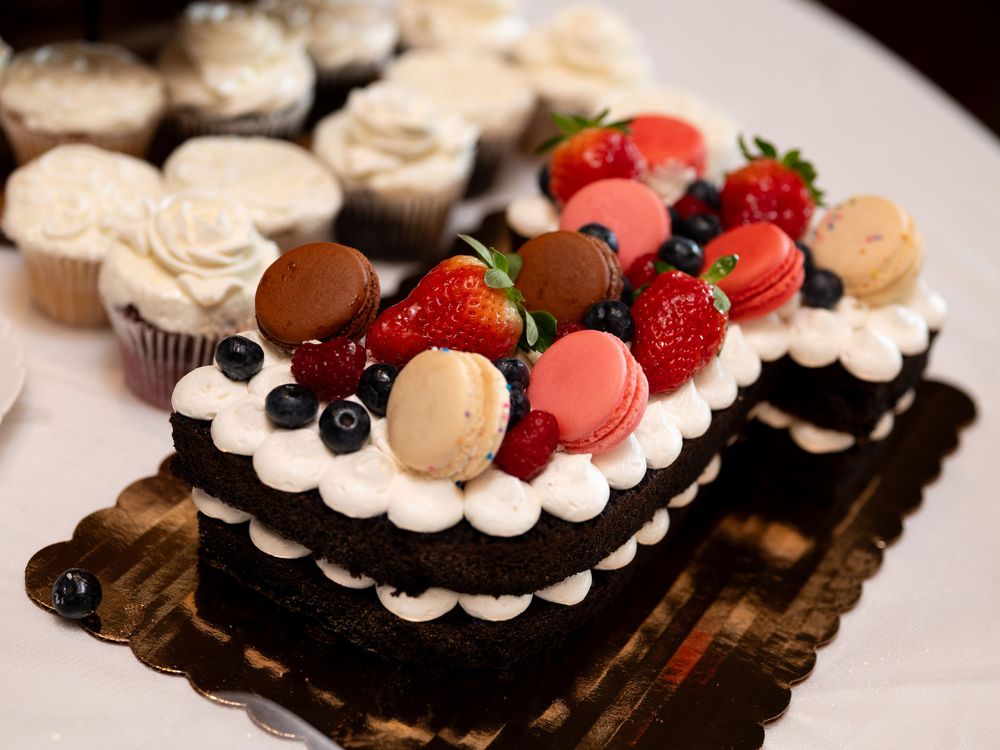An elegant chocolate cake topped with fresh berries, macarons and whipped cream on a dark wooden board.