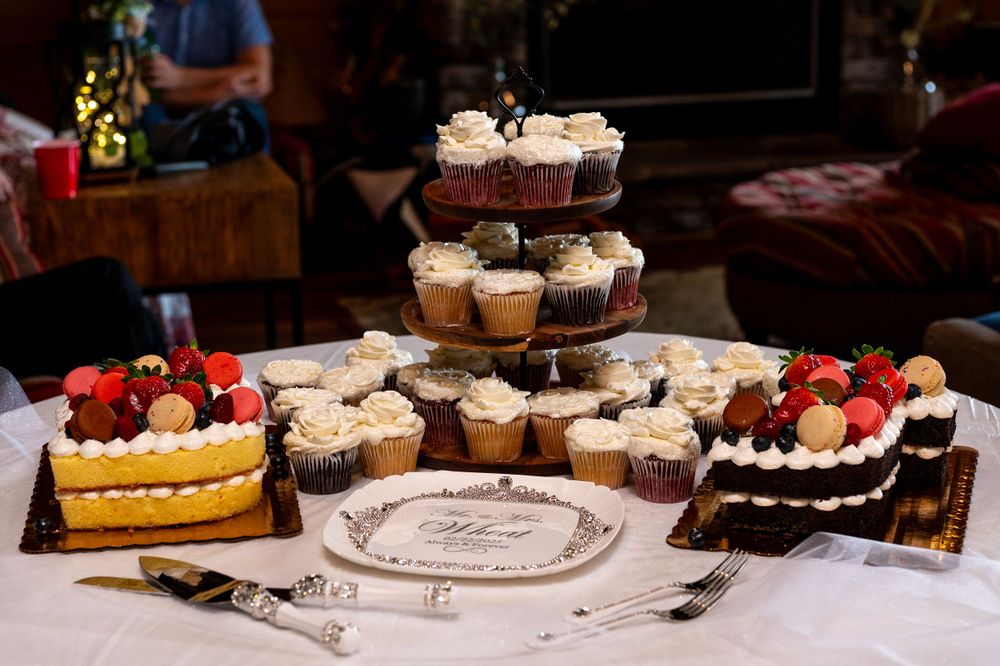 A dessert table with cupcakes on a tiered stand and various cakes displayed on a white tablecloth.