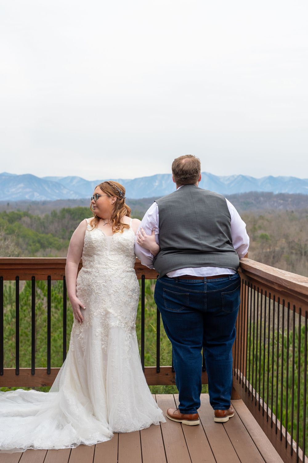 Two people share a tender moment on a wooden deck overlooking a scenic mountain vista on their wedding day.