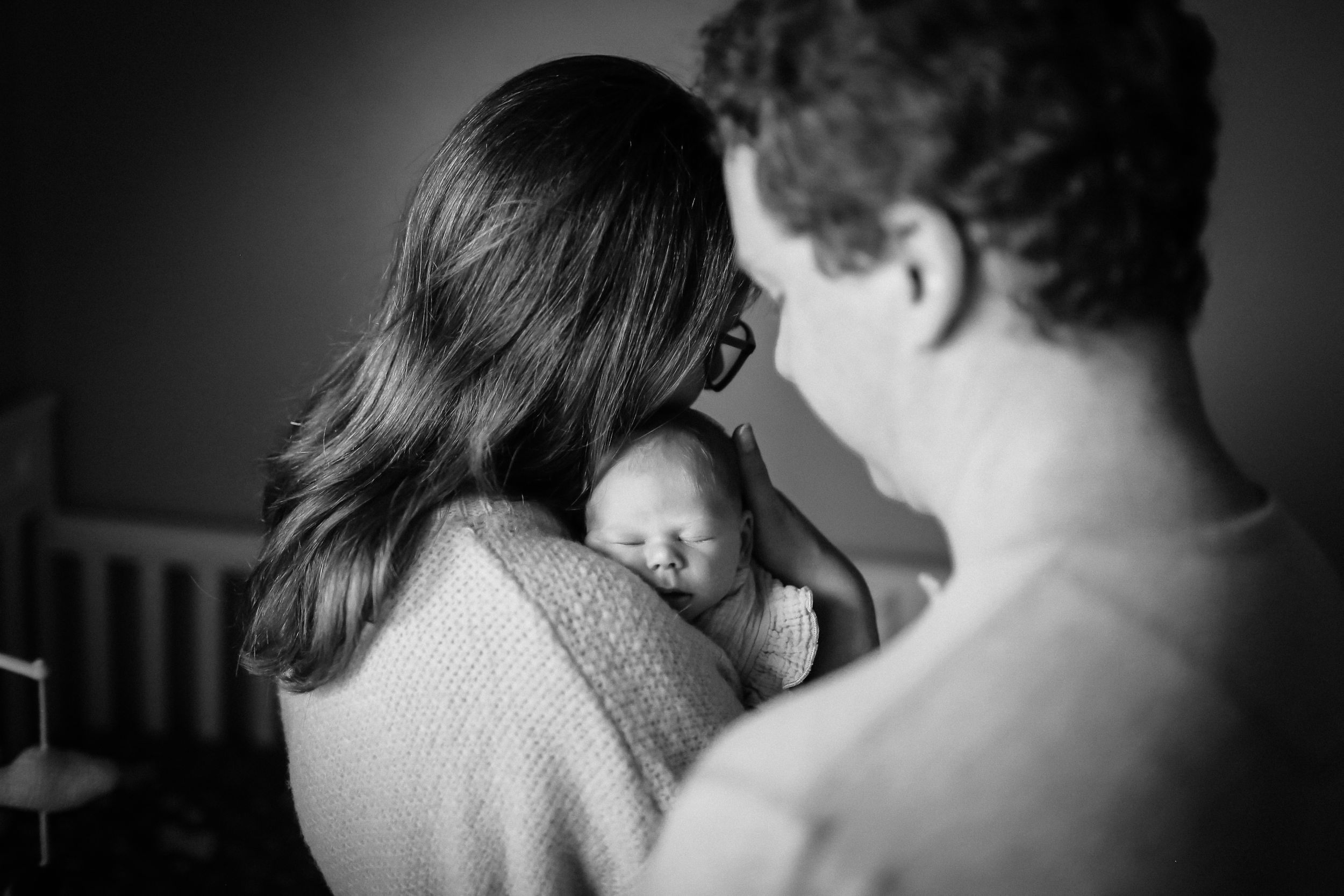 In-home lifestyle session mom and dad snuggling baby girl
