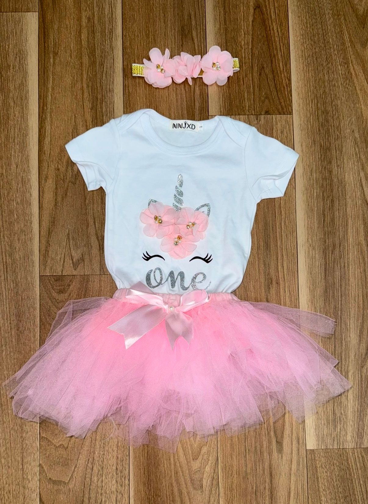 Pink tutu dresses with white bodices laid out on wooden flooring.
