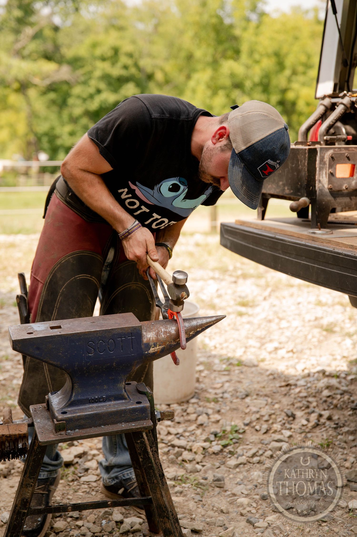 Farrier working on horseshoe shaping using Scott anvil in outdoor setting.