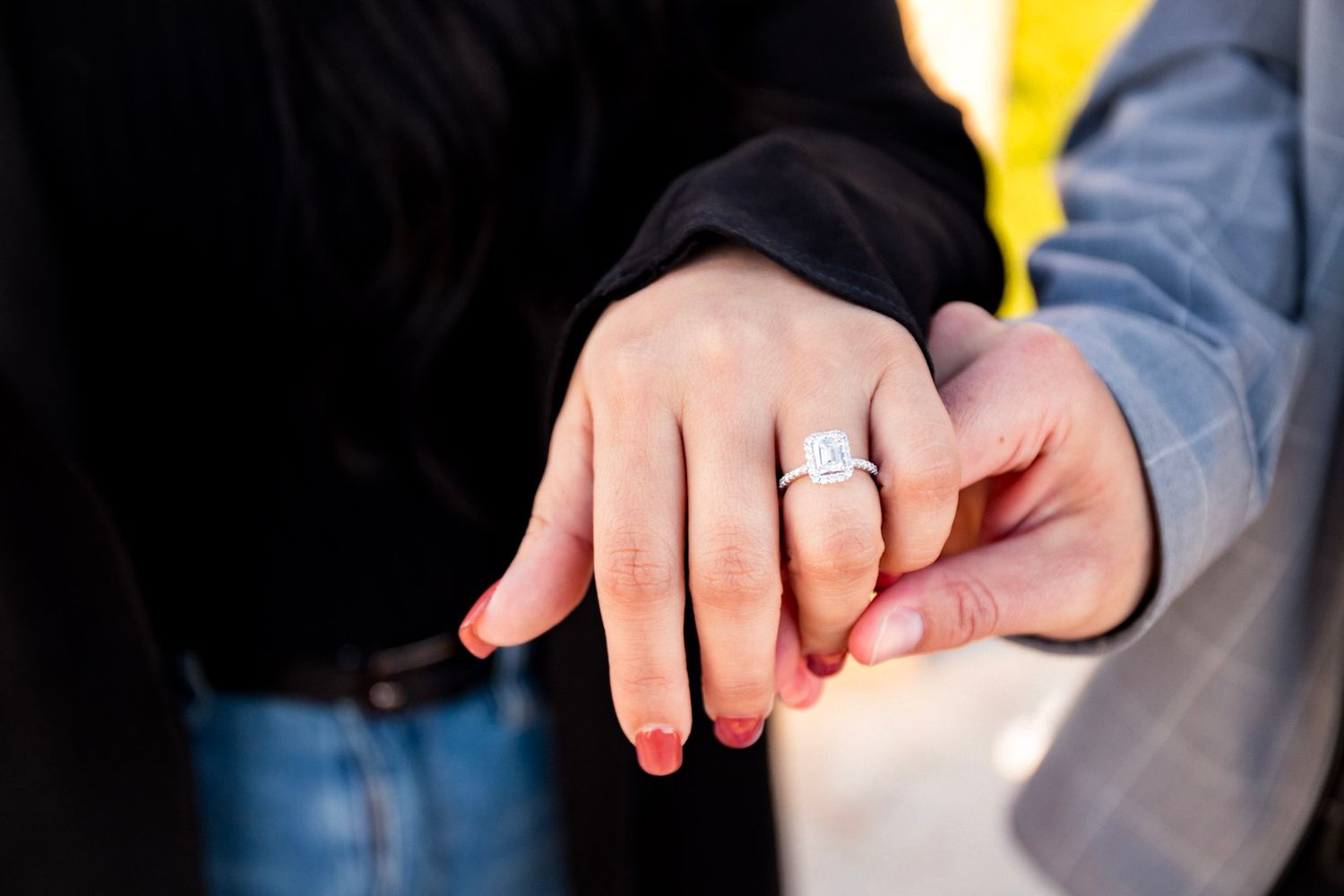 Close-up of an engagement ring on a hand with denim clothing in the background.