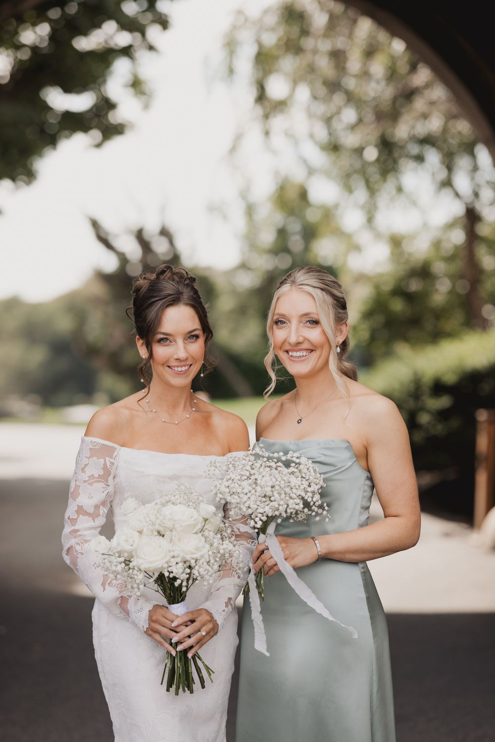 Wedding party poses outdoors holding white floral bouquets in formal attire.