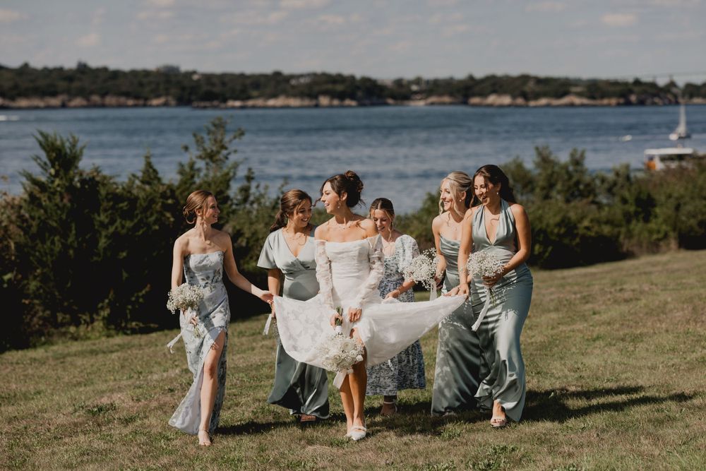 Wedding party walks together on grassy hill overlooking waterfront.