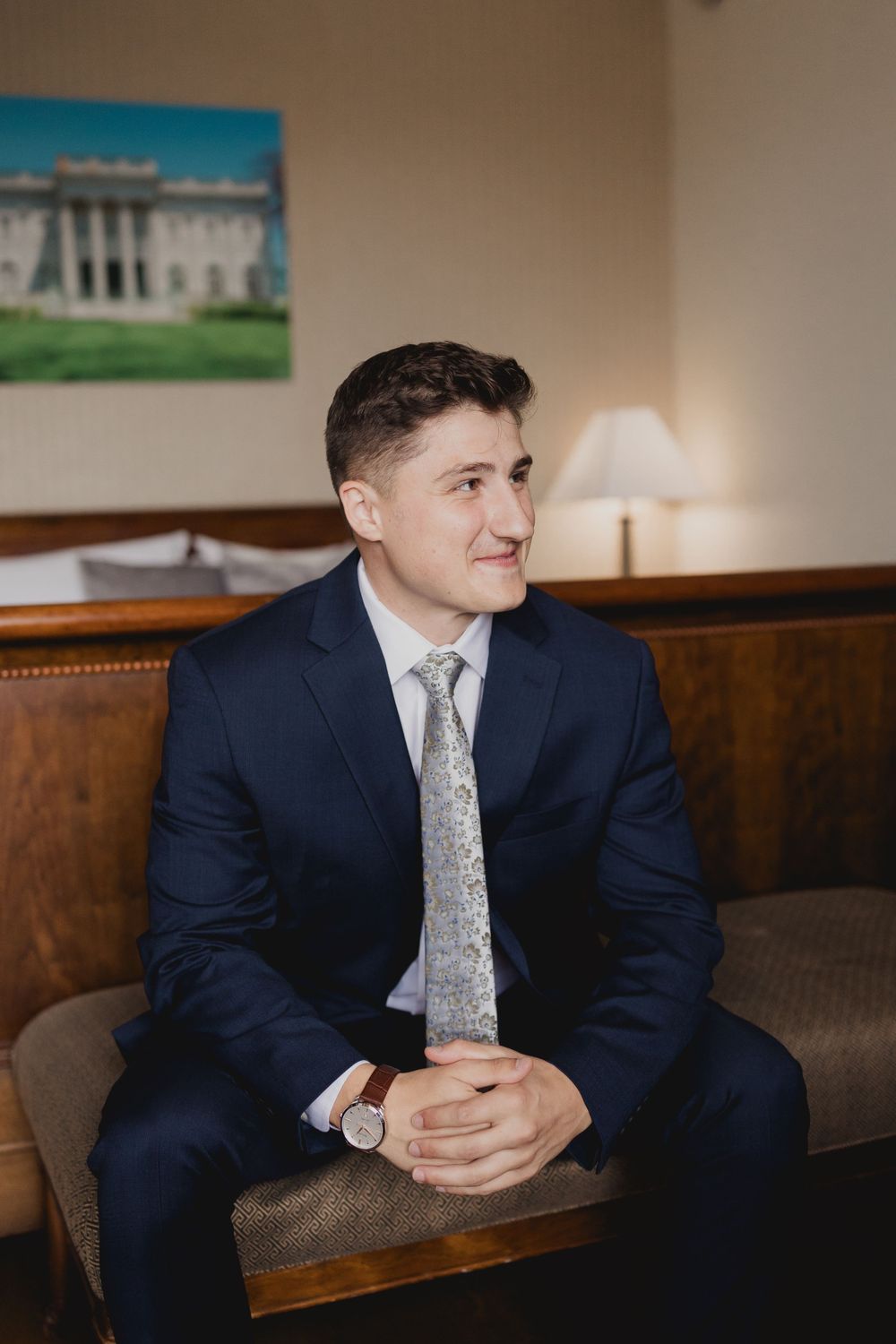 Person in navy suit sits on brown leather couch in formal setting.