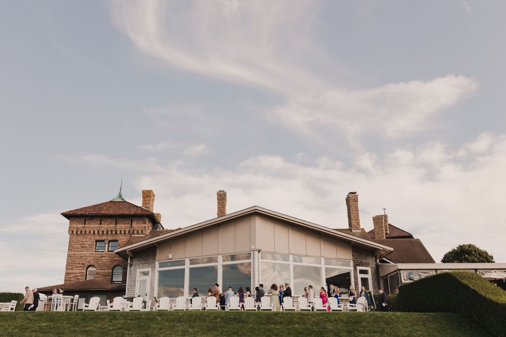 Elegant wedding venue exterior with guests gathered on the lawn under blue skies.