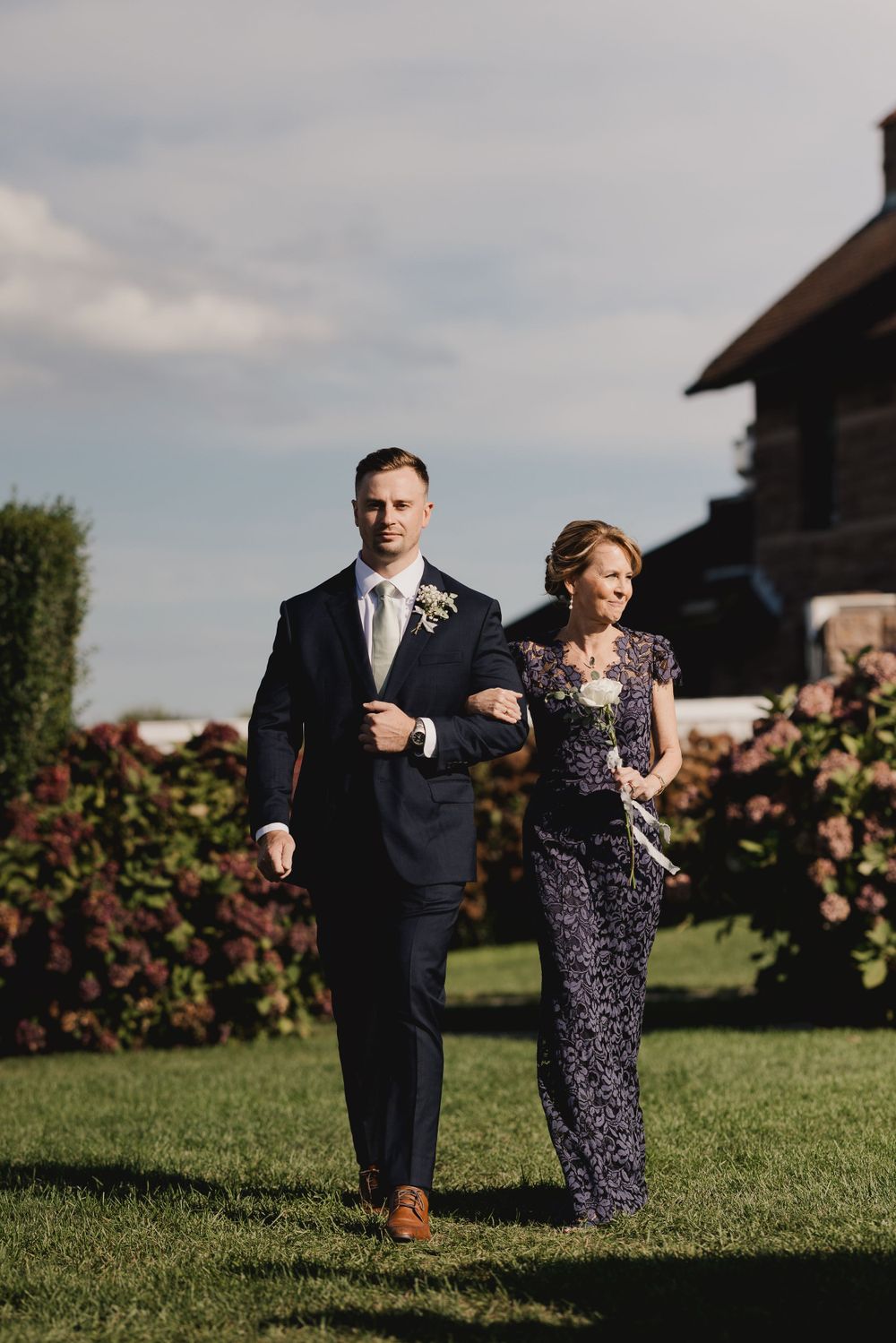 Formal procession of attendants walking across manicured lawn at wedding venue.