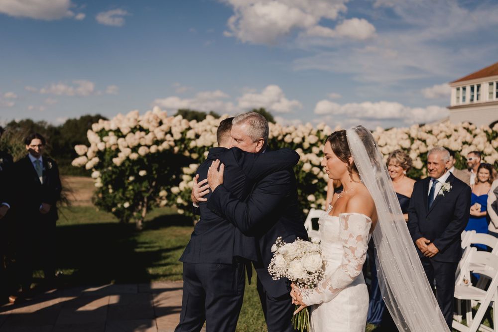 Emotional outdoor wedding ceremony moment against floral backdrop.