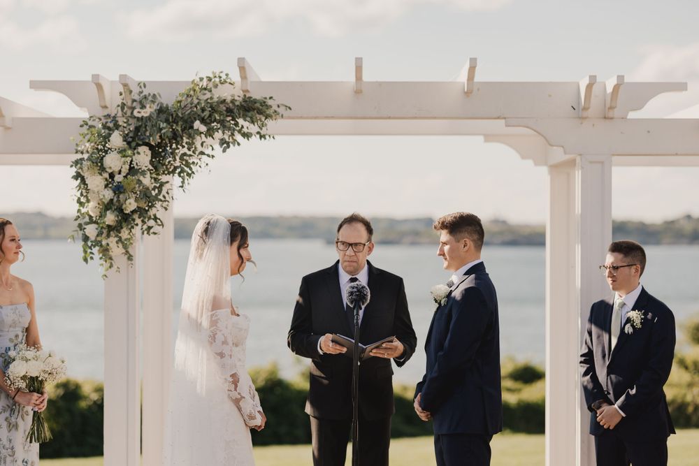 Seaside wedding ceremony under white pergola with delicate floral decorations.