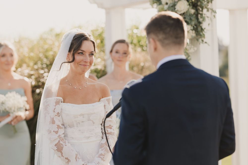 A couple shares an intimate moment during their wedding ceremony under a white floral arch.