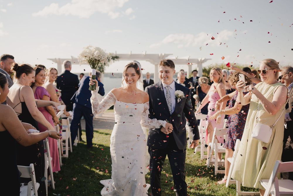Guests toss confetti as newlyweds walk down the aisle at an outdoor waterfront ceremony.