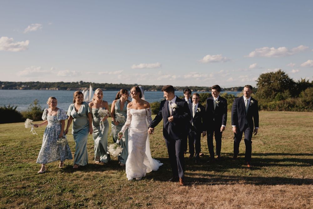 Wedding party poses for photos on a hilltop overlooking a scenic waterfront.