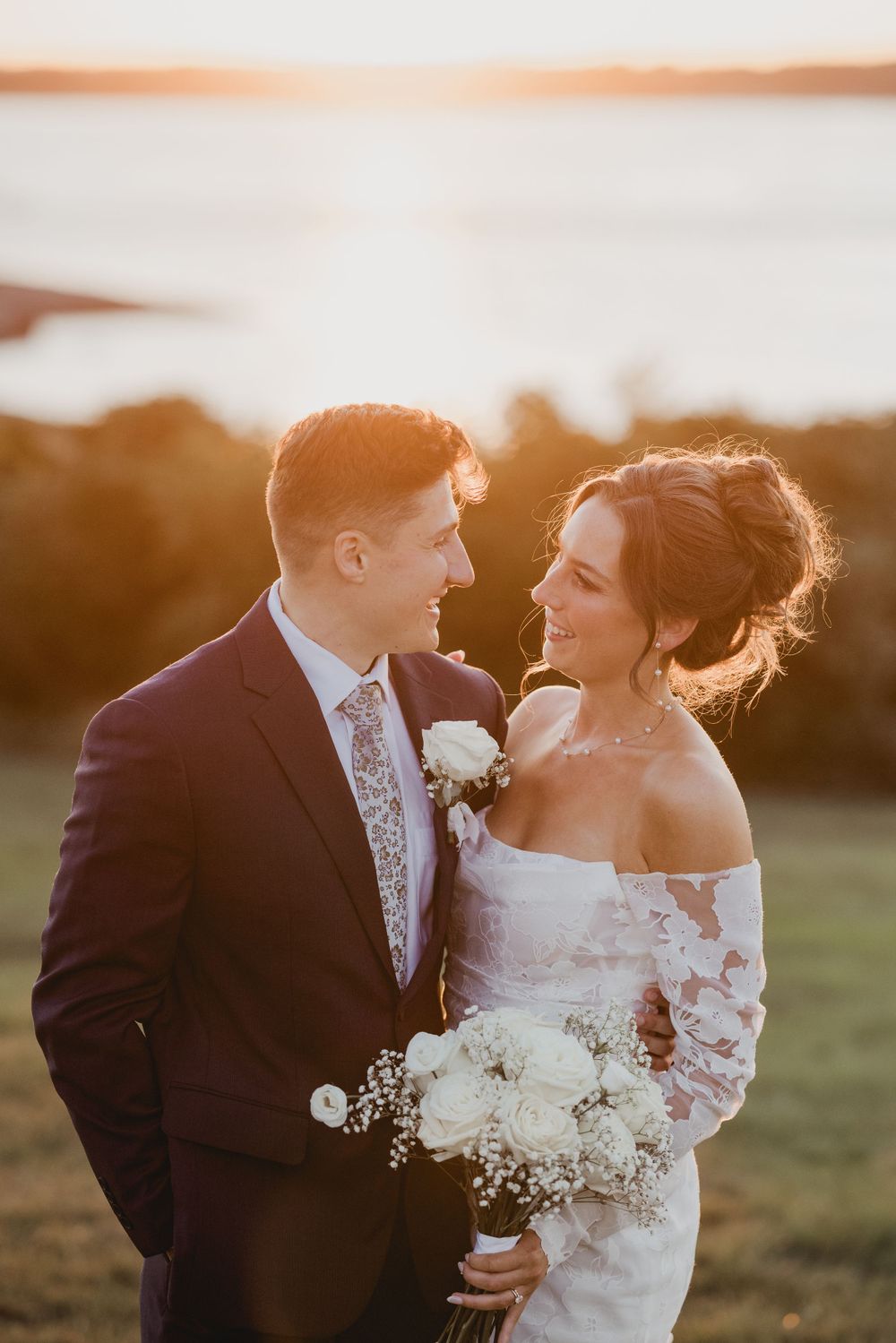 Couple shares intimate moment during sunset wedding photoshoot with ocean backdrop.