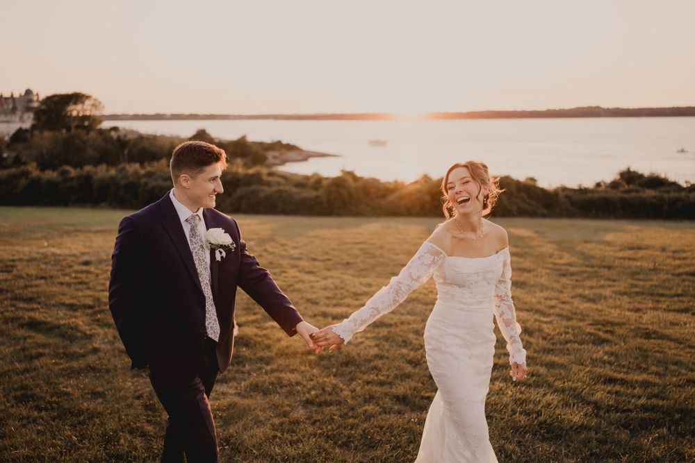 Couple walks hand in hand across hilltop field during golden hour.