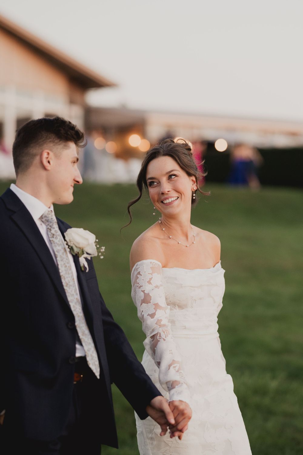 Couple in formal wedding attire shares joyful moment on lawn at dusk.