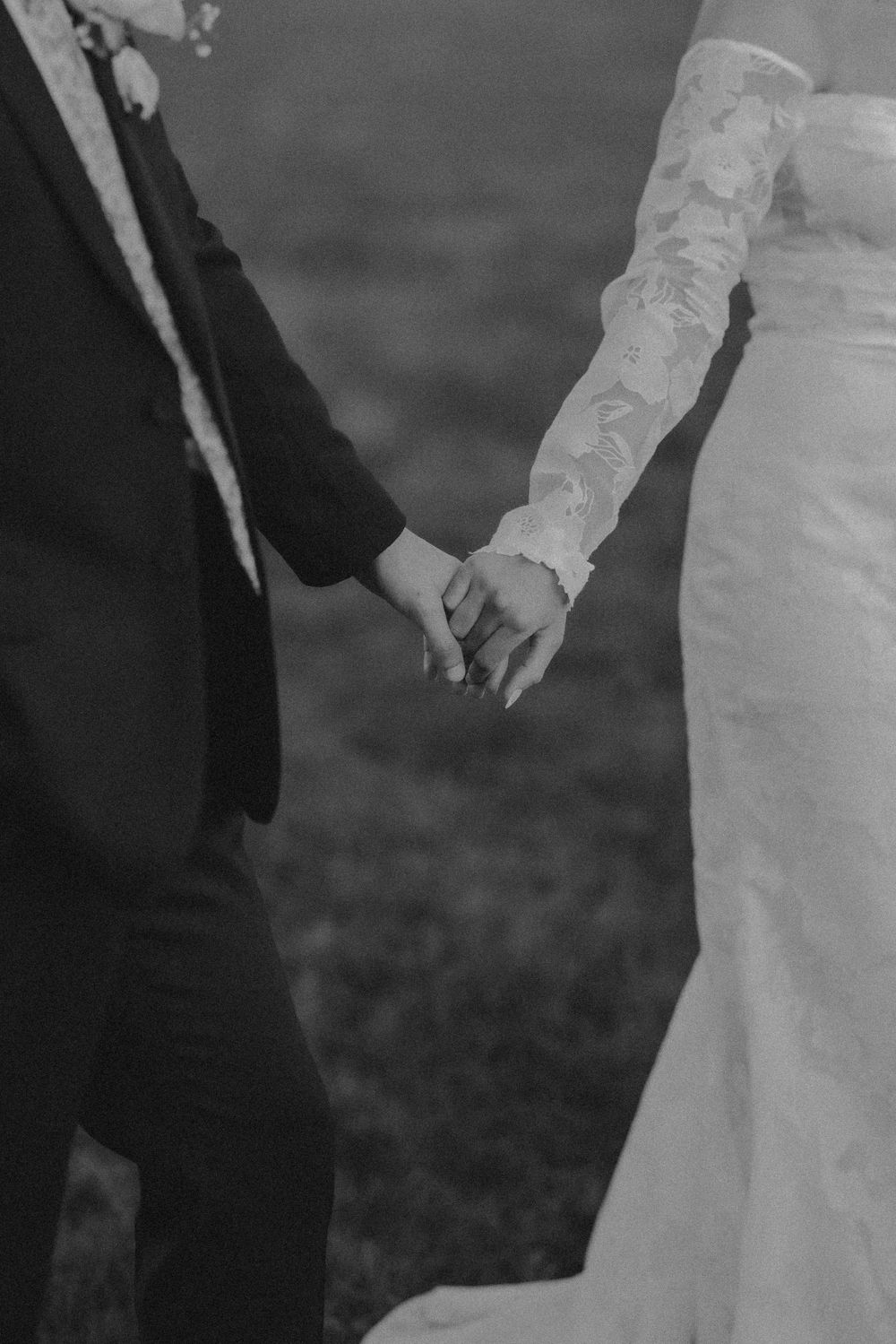 Black and white detail shot of couple holding hands showing lace sleeve and formal attire.
