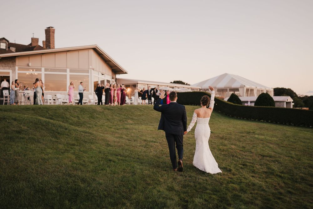 Wedding guests gather on a lawn outside a venue with mountain views at dusk.