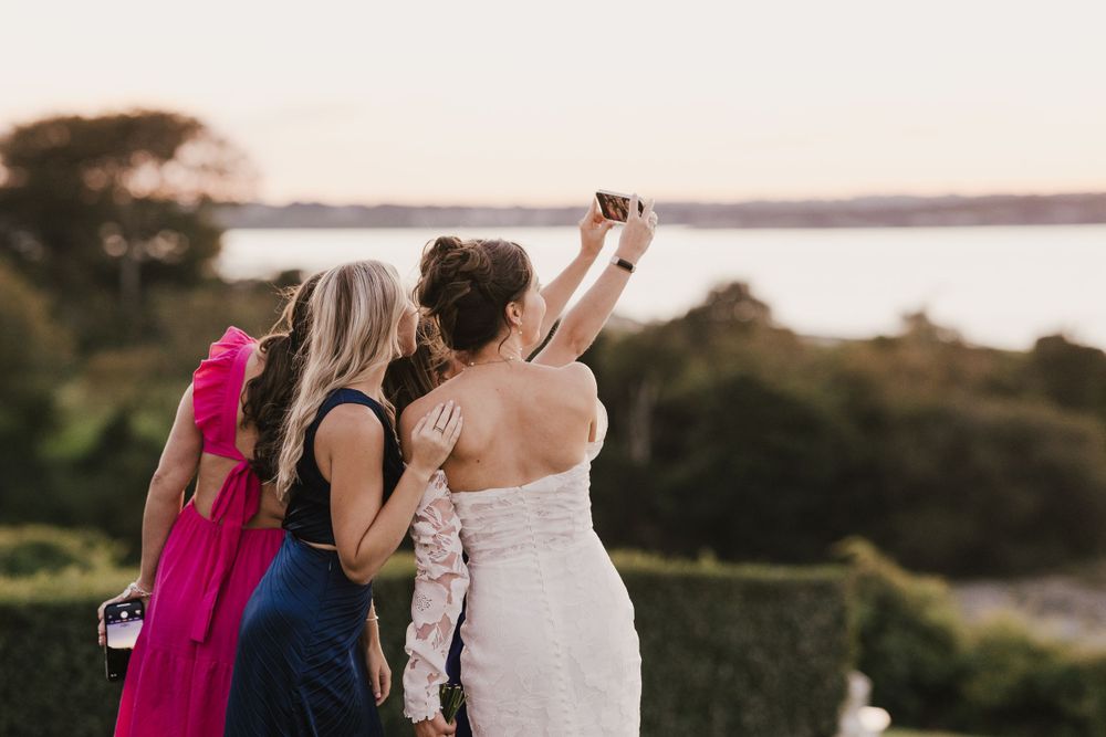 Wedding attendees take photos at sunset with an ocean view in the background.