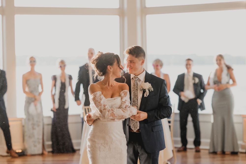A couple shares their first dance surrounded by wedding guests in an elegant ballroom.