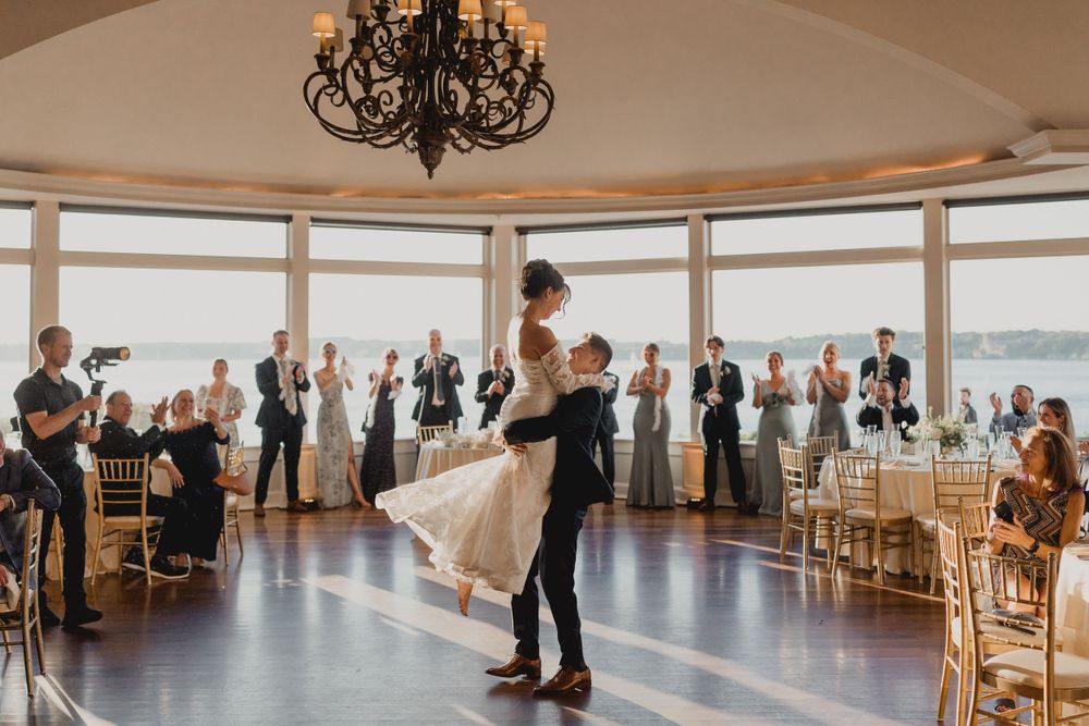 Newlyweds perform their first dance in a sunlit ballroom while guests watch from the sides.