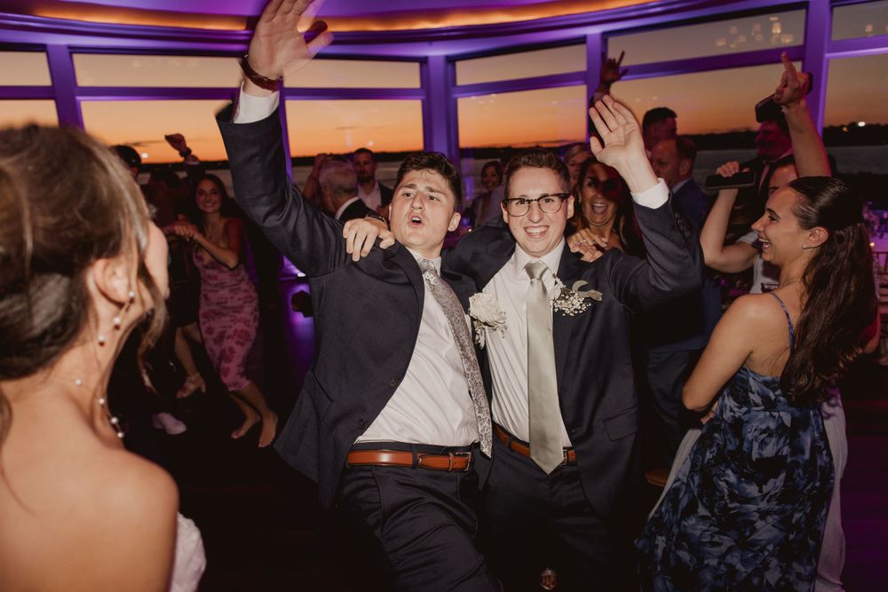 Crowd of party guests dancing with raised arms under dramatic event lighting.