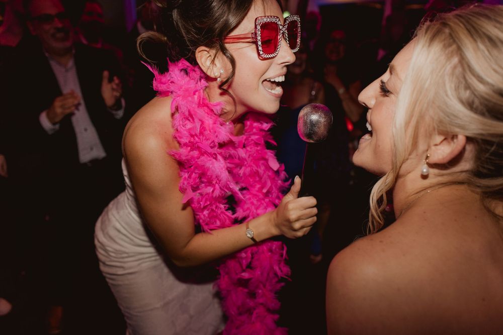 Dancers wearing bright pink accessories celebrating at a nighttime wedding reception.