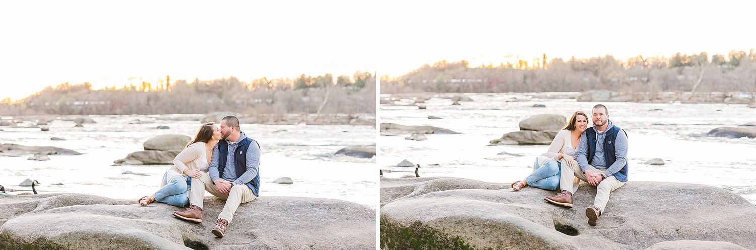 A couple sits together on a rocky beach shoreline at sunset during an engagement photoshoot.