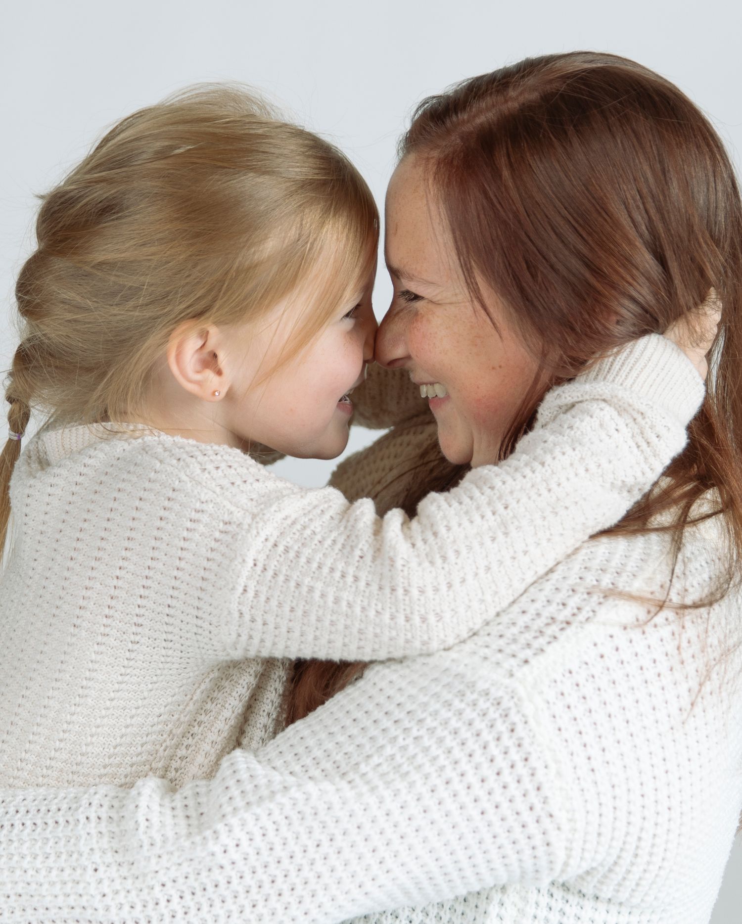 Two people in white knit sweaters share an intimate loving moment with their foreheads touching.
