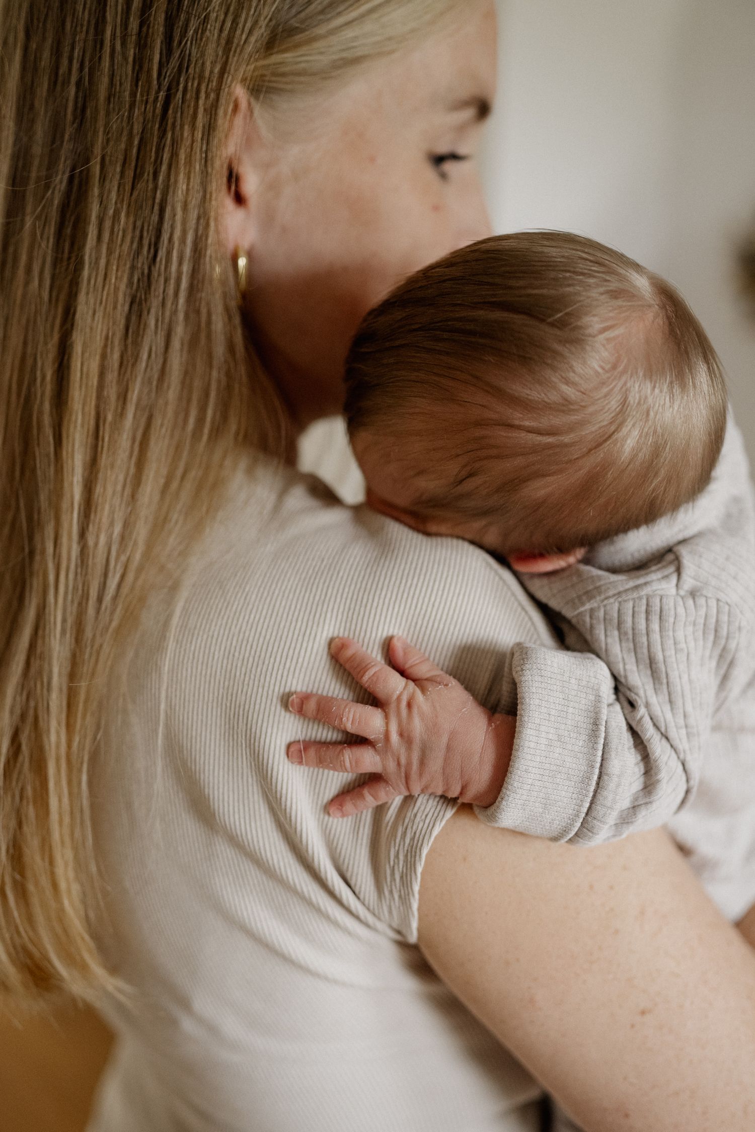 A tender moment captured showing a baby in a cream sweater being held close against someone wearing white.