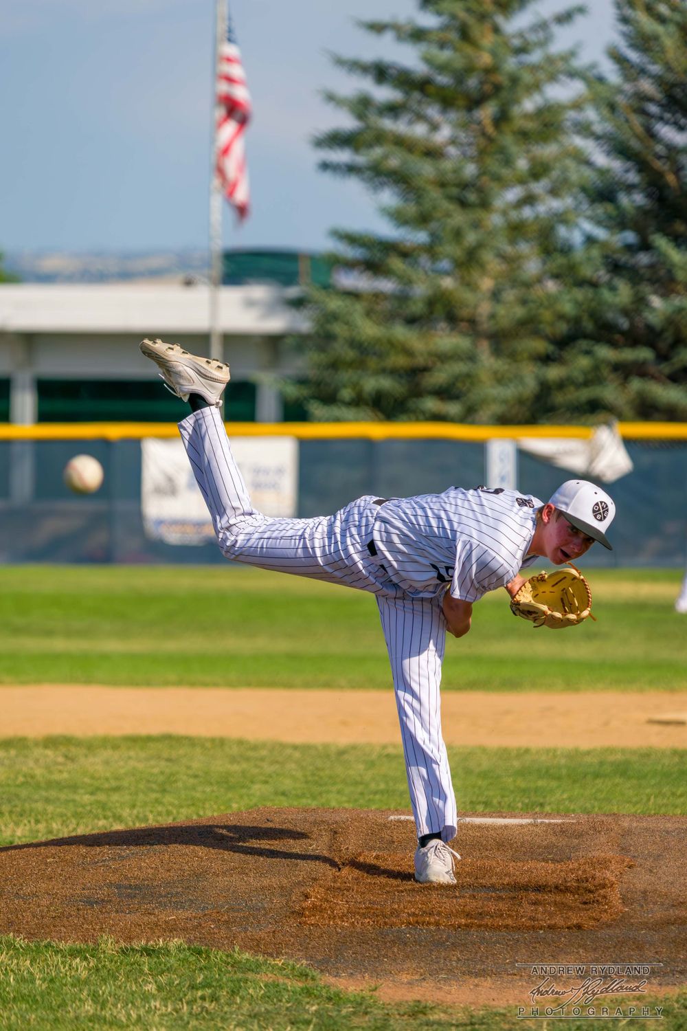 Baseball pitcher following through on delivery with American flag in background.