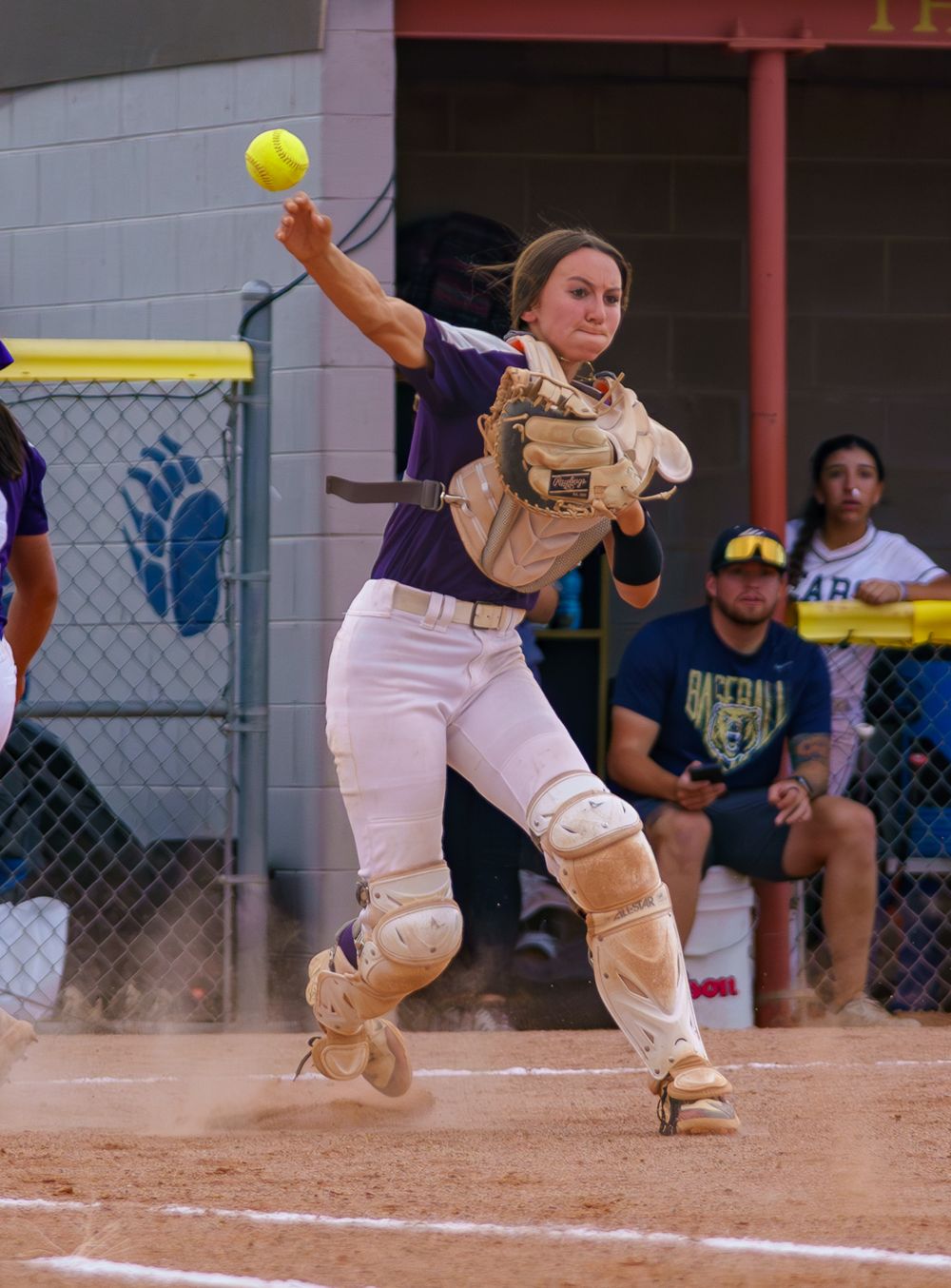 A catcher in protective gear preparing to catch a softball at home plate in a motion sequence.
