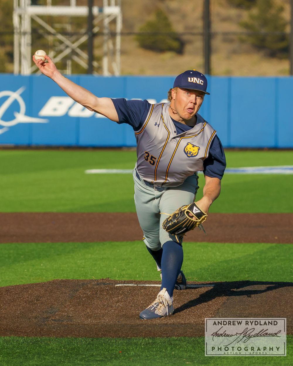 Baseball pitcher in mid-delivery motion on the mound during sunset game.