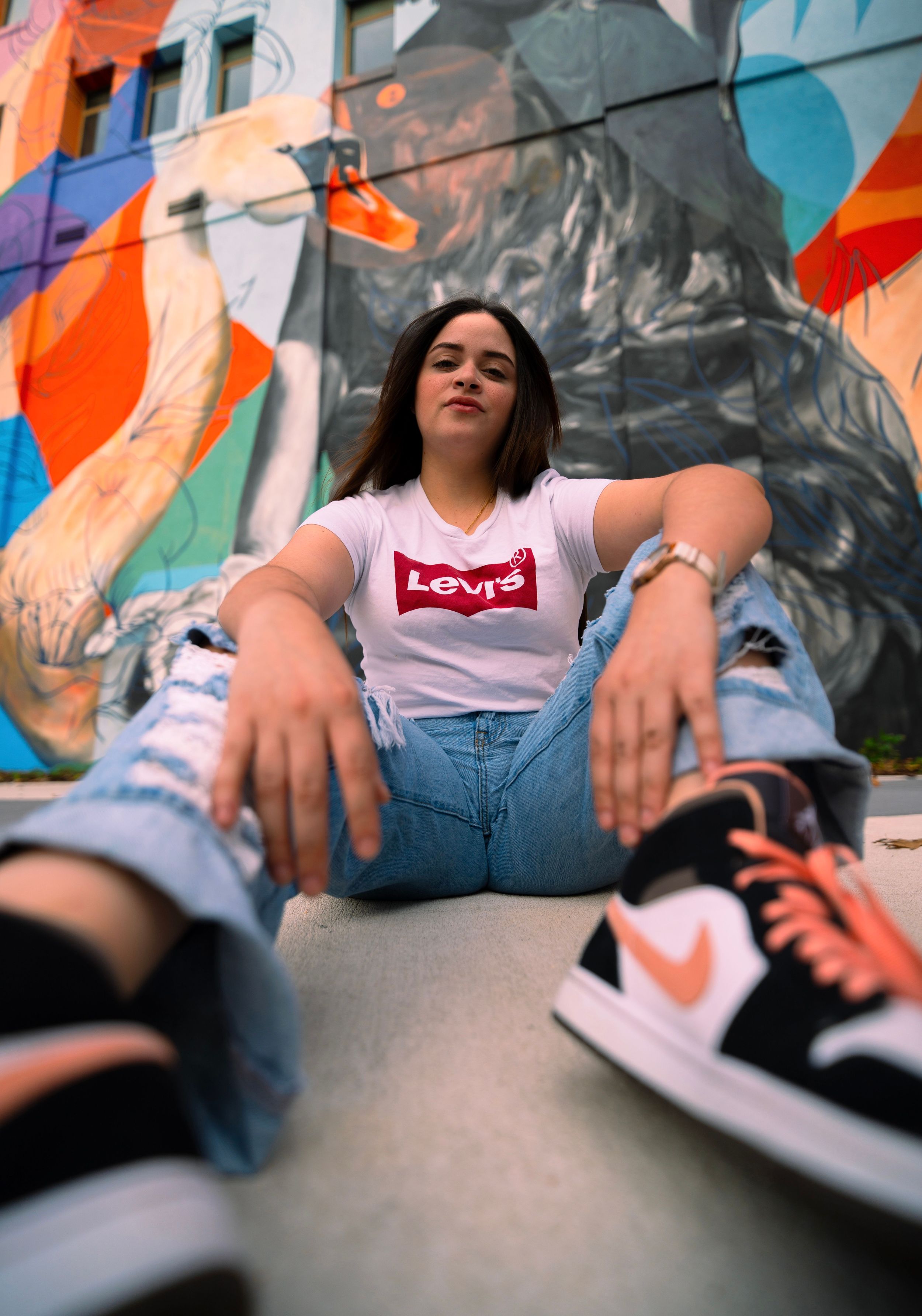 Street style fashion photo featuring Levi's t-shirt, ripped jeans and Nike sneakers against colorful mural.