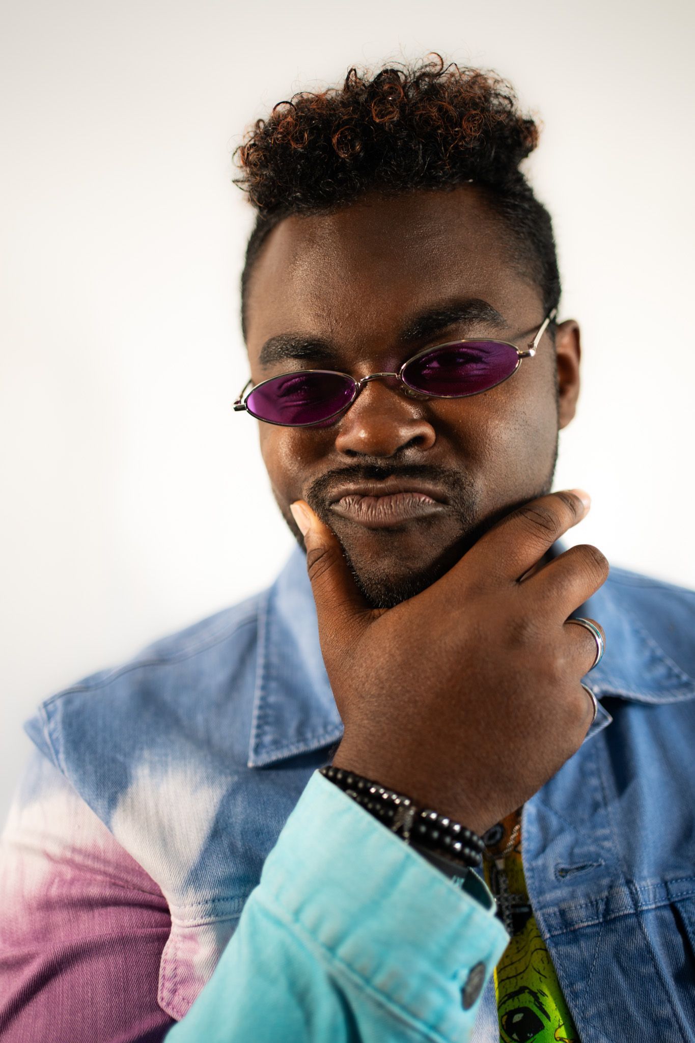 Stylish portrait wearing tinted glasses and color block denim jacket against white background.