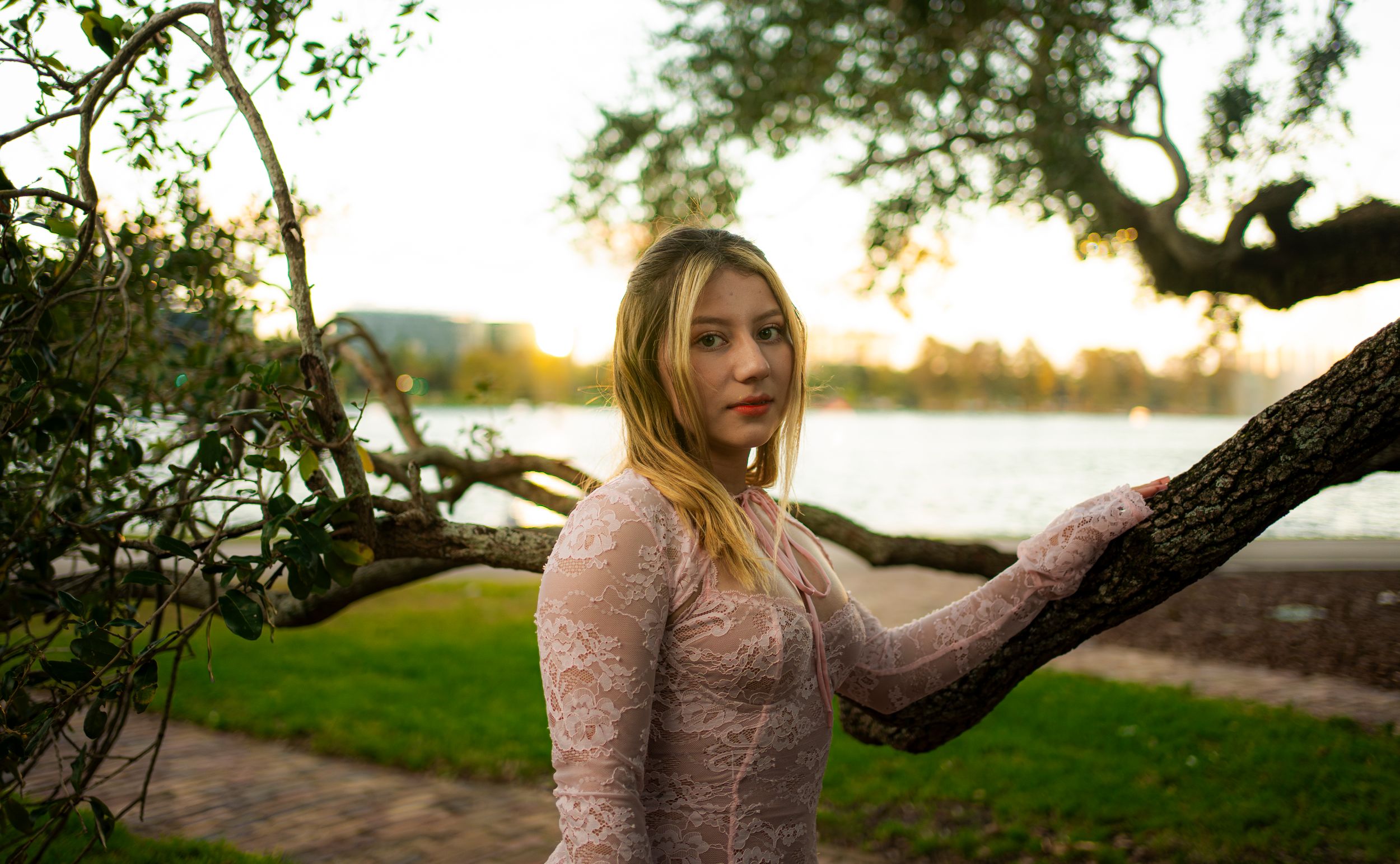 Portrait at golden hour by a lake with sunlight filtering through trees.