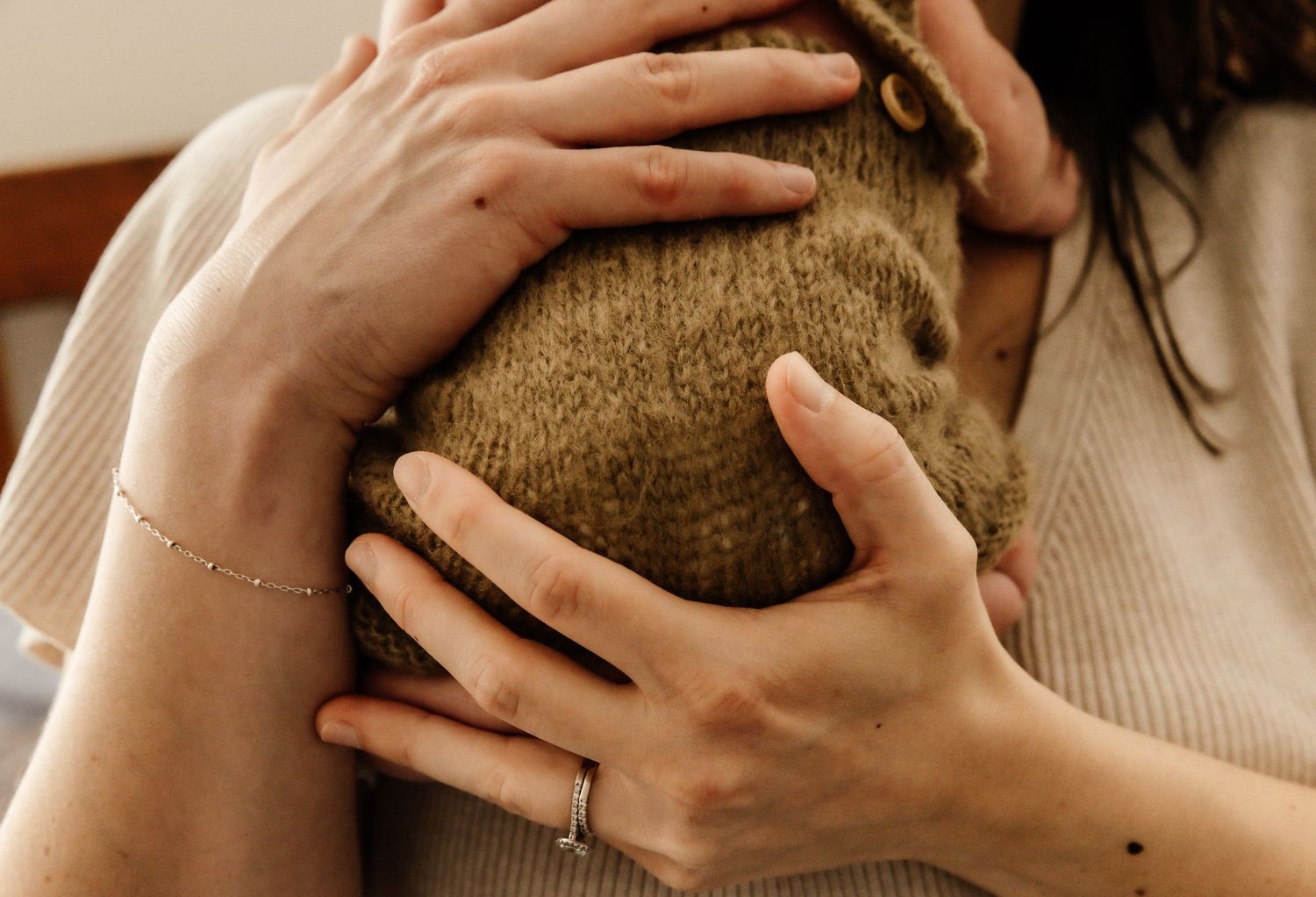 Person wearing beige sweater holds someone close in an intimate embrace, showing delicate hands and bracelets.