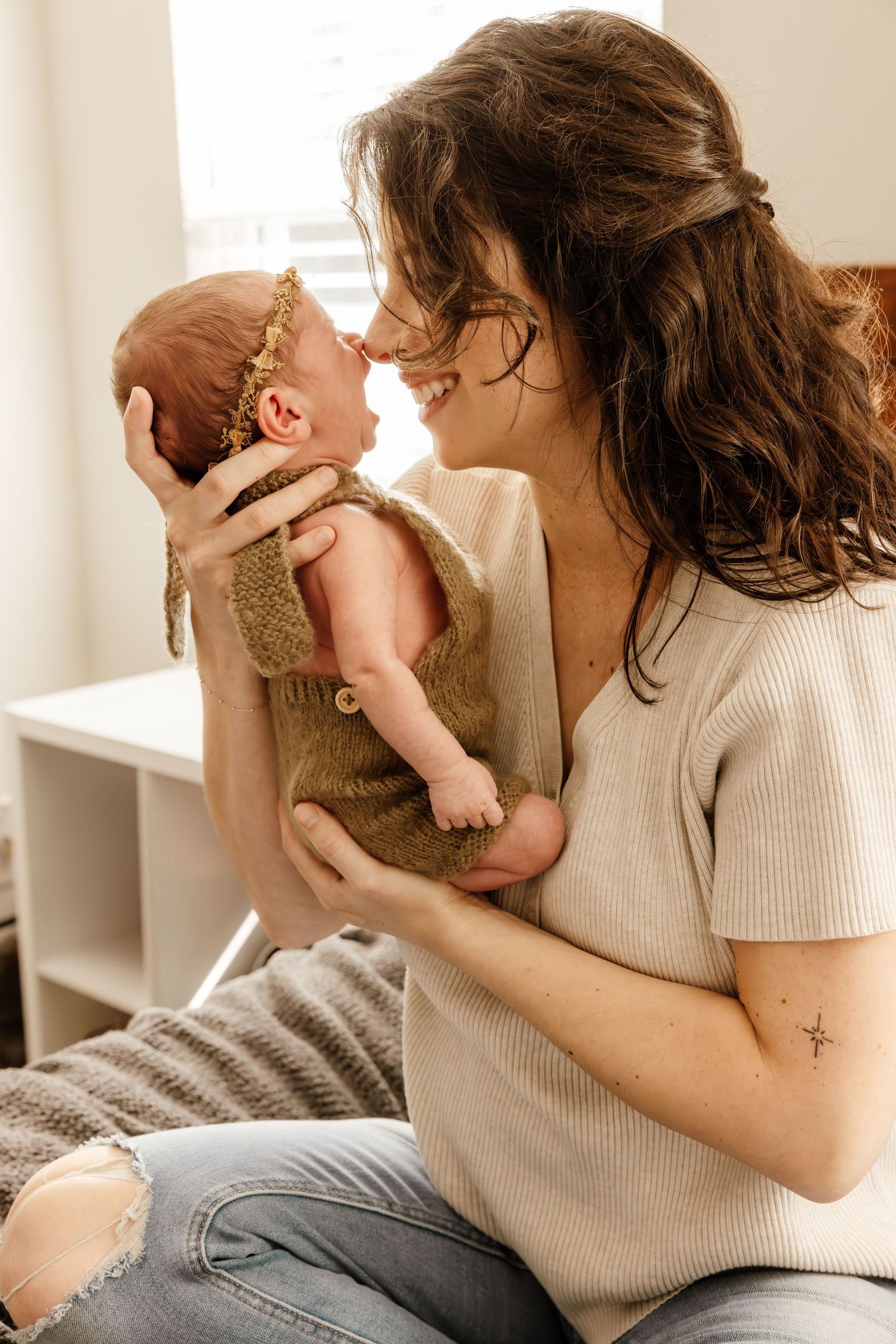 Candid moment showing gentle maternal bonding with a small baby wearing a gold crown headband in a cozy indoor setting.