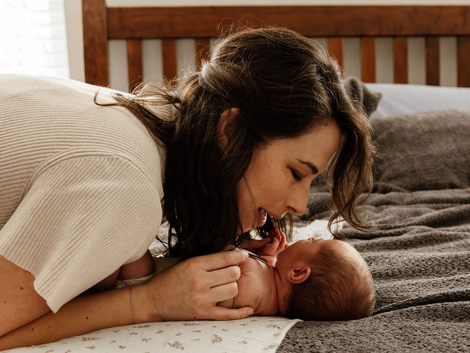 A parent lies on a bed sharing a tender moment with their newborn baby in a cozy bedroom setting.