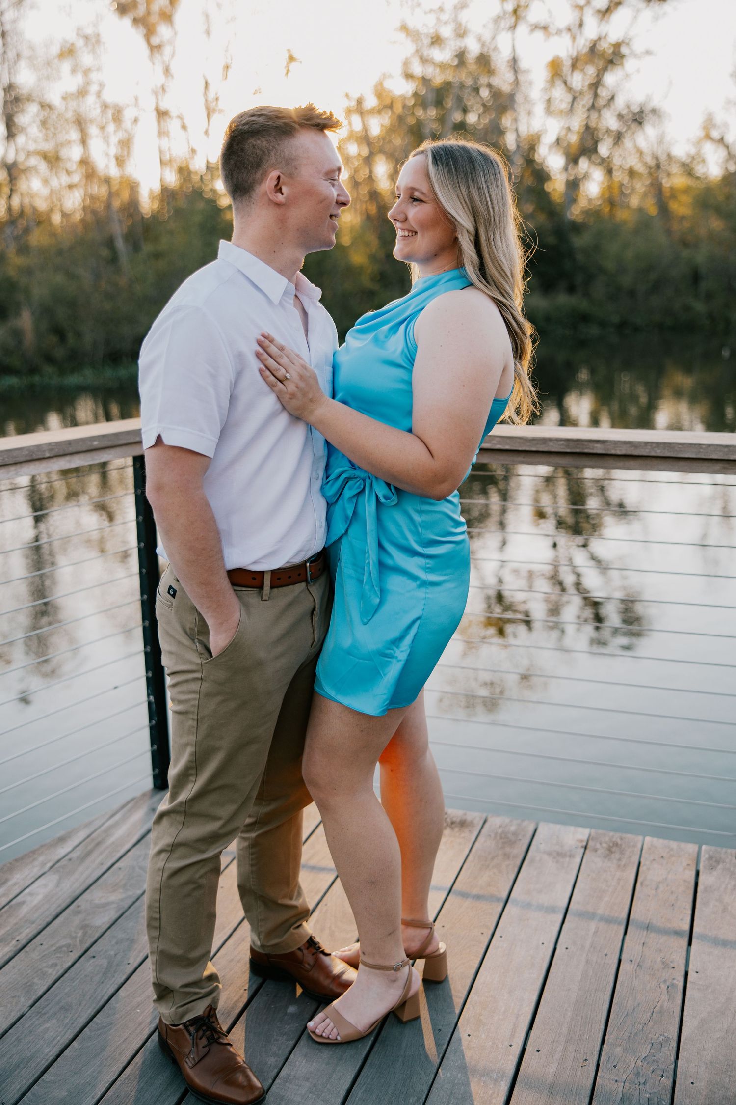 A couple shares a romantic moment on a wooden dock by a lake at sunset while dressed in casual summer attire at Bonnet Springs Park