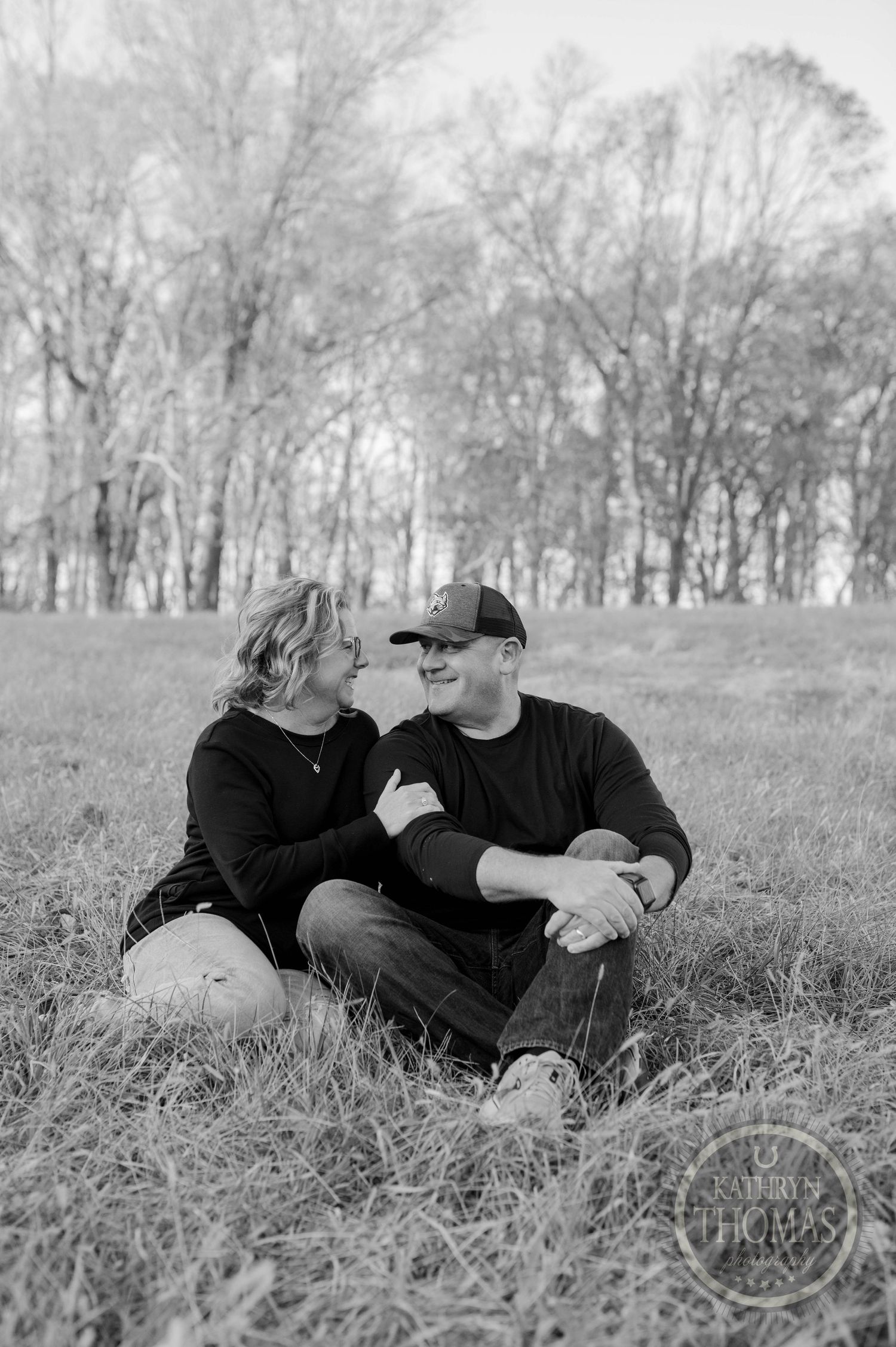 Black and white portrait of couple sharing intimate moment on grassy hillside.