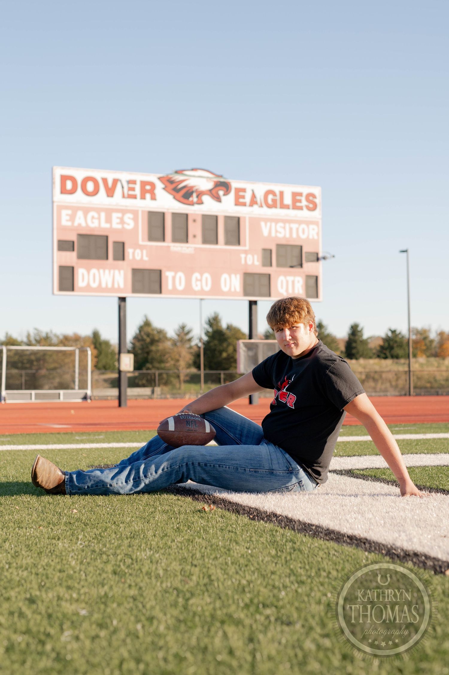 Player relaxes with football by Dover Eagles scoreboard on field during golden hour.
