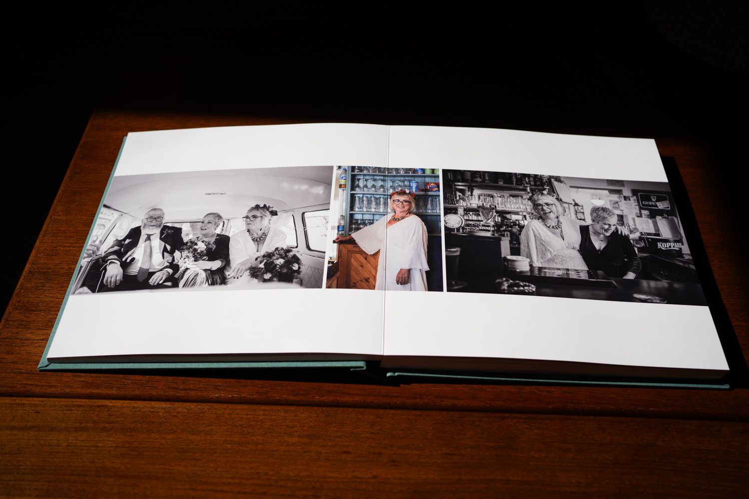 A photo album lying open on a wooden table displays a series of black and white photographs arranged in a row.