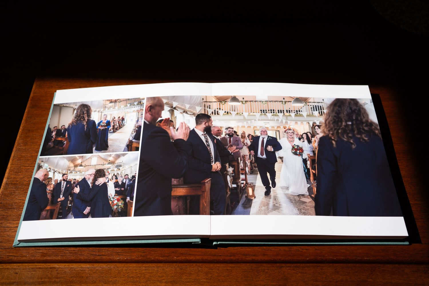A wedding photo album lies open on a wooden table showing ceremony photographs in a spread layout.