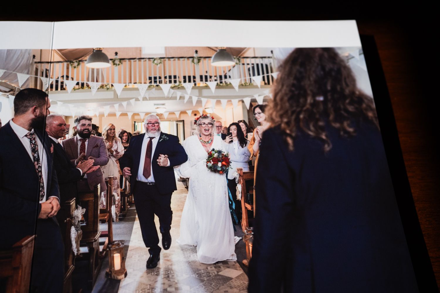 A wedding procession walks down a church aisle surrounded by guests in formal attire.