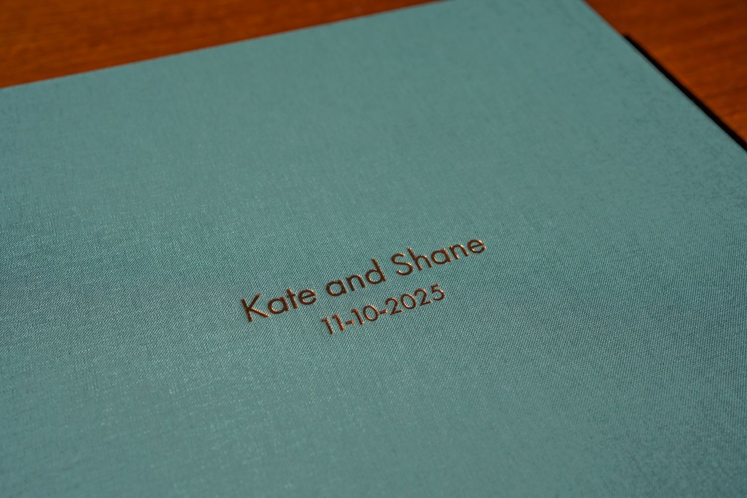 A turquoise photo album cover with embossed text showing names and dates.