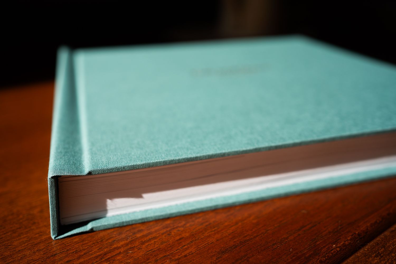 A teal hardcover book with bookmark tabs sits on a dark wooden surface, photographed in close-up.