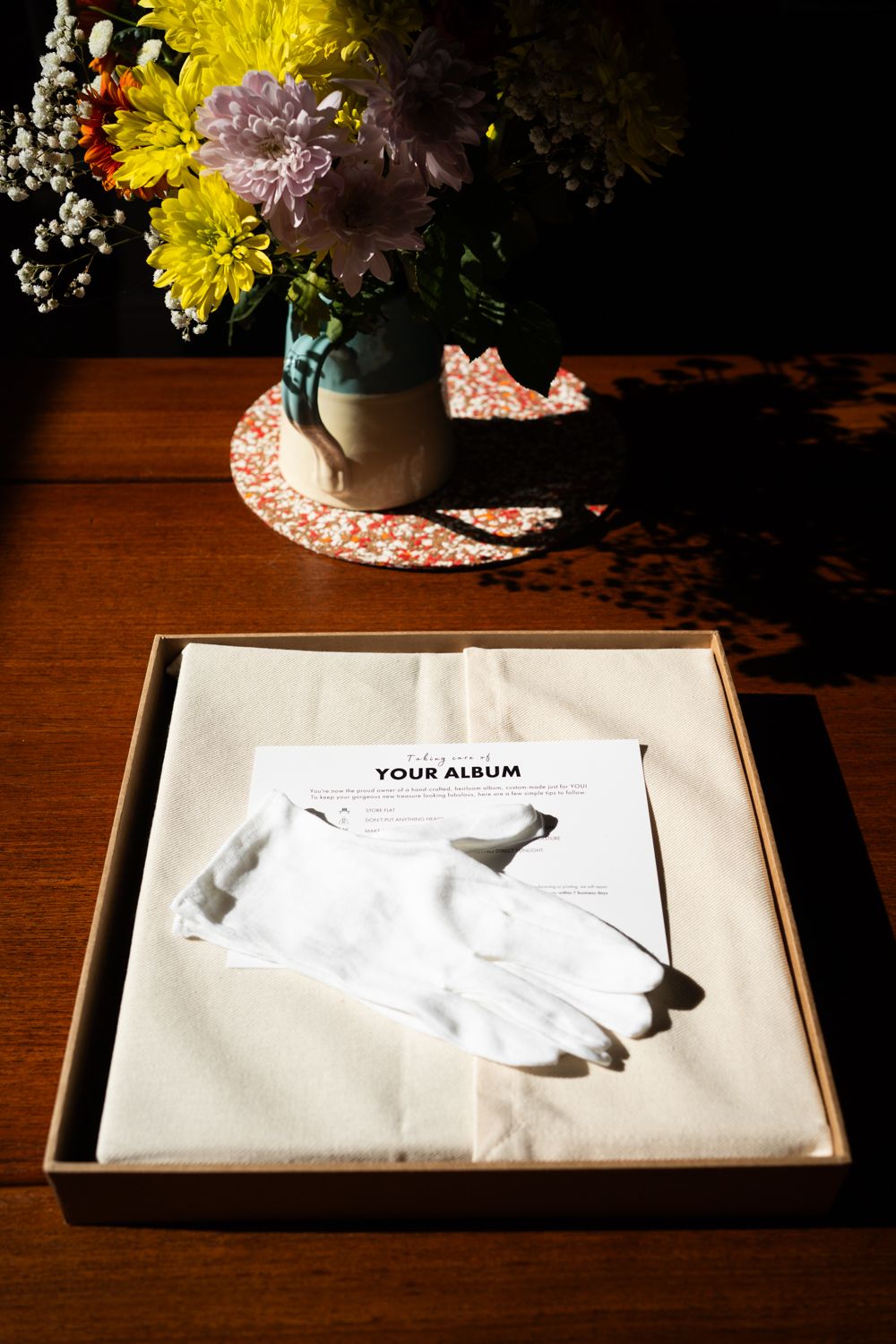 White photo album box with floral arrangement in vase on wooden surface.