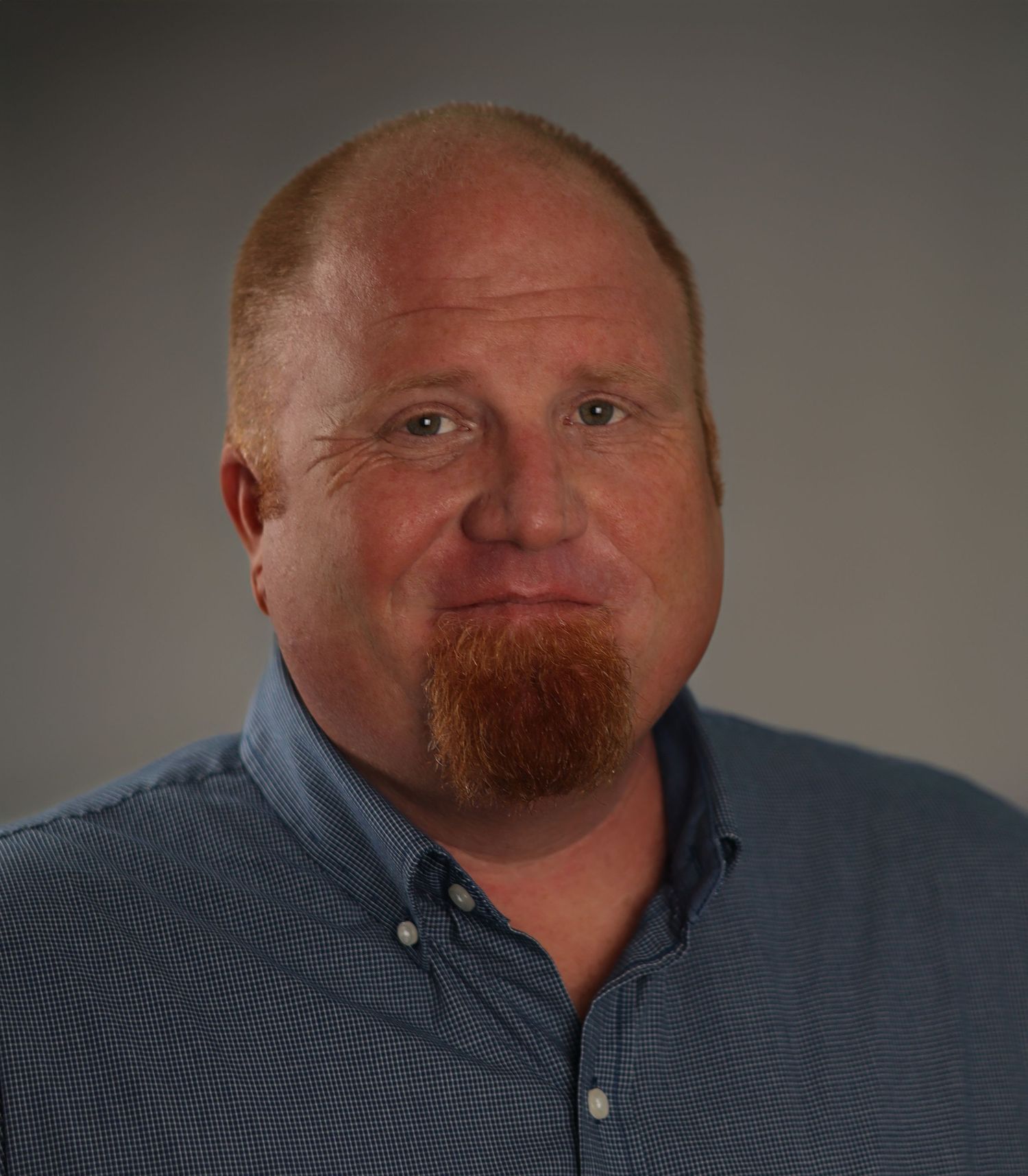 Professional headshot portrait of a person in a blue button-down shirt against a gray background.